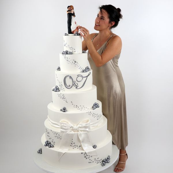 קארין עמנואל עם עוגת חתונה ענקית ב-7 קומות לבן עם כסוף מעוצבת בבצק סוכר ודמויות חתן וכלה מפוסלים בעבודת יד